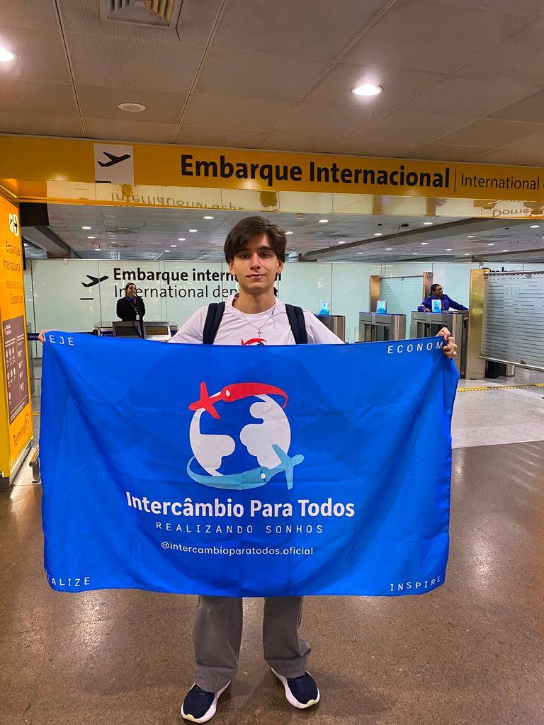 João Mello no aeroporto com a bandeira da Intercâmbio Para Todos