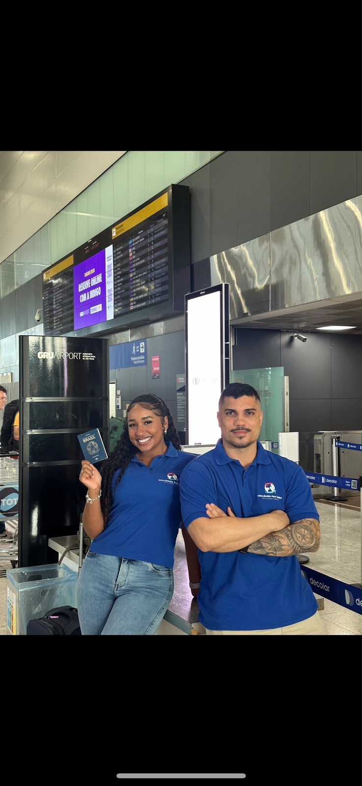 Duas pessoas da equipe da IPT no Aeroporto de Guarulhos, uma delas segurando um passaporte brasileiro